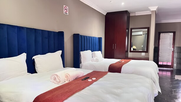 A hotel room with two beds, each with white linens and a red accent. There is a large mirror and a wardrobe in the room. - Novel Enterprises Bed and Breakfast (Rustenburg)
