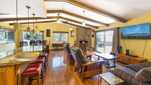 Amplia sala de estar con chimenea de piedra, muebles de madera y grandes ventanales que ofrecen vistas al exterior.