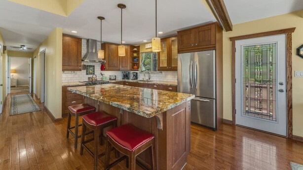 Cocina con isla de granito, armarios de madera y electrodomésticos de acero inoxidable, además de una puerta con reja metálica.