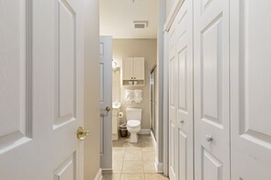 A narrow hallway leading to a bathroom with a toilet, cabinets, and a trash can.