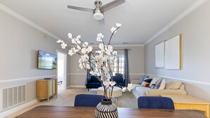 A modern living room with a dining table, a vase with flowers, a ceiling fan, and a TV on the wall. - Stylish Golf  Beach Getaway (Myrtle Beach)