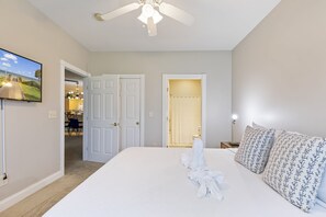 A hotel room with a large bed, a ceiling fan, a TV, and a bathroom visible through an open door.