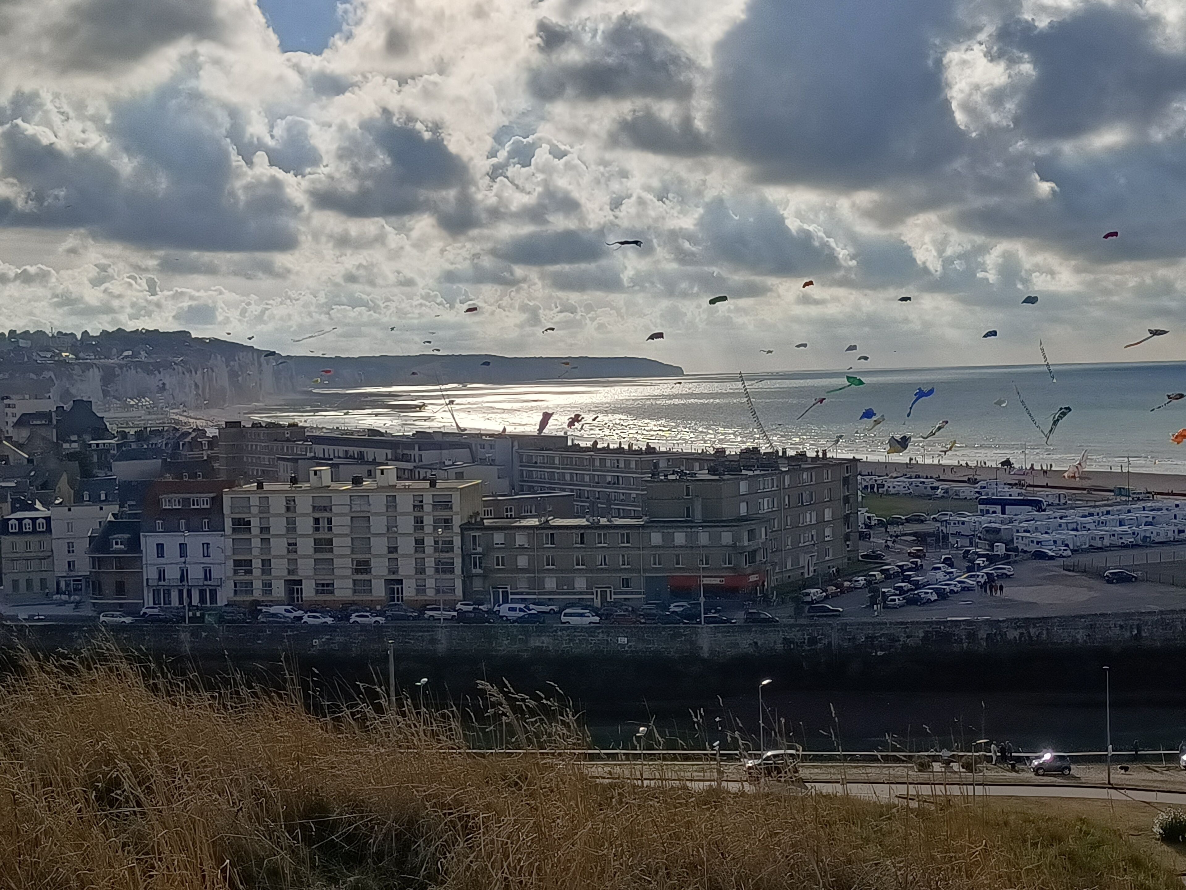 A coastal cityscape with buildings, a parking area, and a view of the sea.