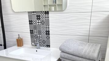 A bathroom with a white sink, a mirror, a patterned tile backsplash, and a wooden towel rack with folded towels.