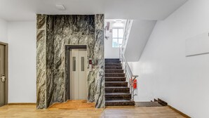 A modern interior with a marble wall, wooden flooring, and a staircase leading to an upper level. - Rohaan Inns - UPAR Hotels Ashok Nagar (Chennai)