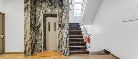A modern interior with a marble wall, wooden flooring, and a staircase leading to an upper level.
