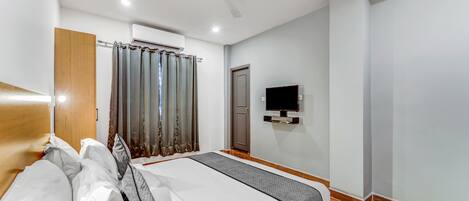 A hotel room with a bed, a ceiling fan, an air conditioning unit, a television, and a door.