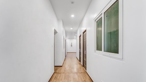 A narrow hallway with wooden flooring and white walls, leading to a door at the end. - Rohaan Inns - UPAR Hotels Ashok Nagar (Chennai)