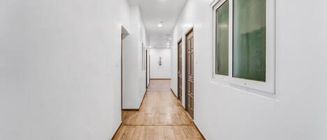 Un couloir étroit, doté d’un plancher en bois et de murs blancs, qui mène à une porte au fond.