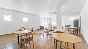A spacious room with wooden flooring, multiple tables and chairs, and large windows allowing natural light. - Rohaan Inns - UPAR Hotels Ashok Nagar (Chennai)