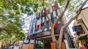 A multi-story building with a checkered facade, a tree in front, and a gated entrance. - Rohaan Inns - UPAR Hotels Ashok Nagar (Chennai)
