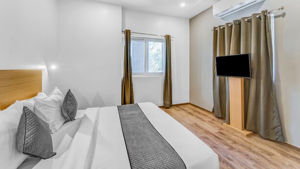 A hotel room with a bed, a TV, an air conditioner, and a window with curtains. - Rohaan Inns - UPAR Hotels Ashok Nagar (Chennai)