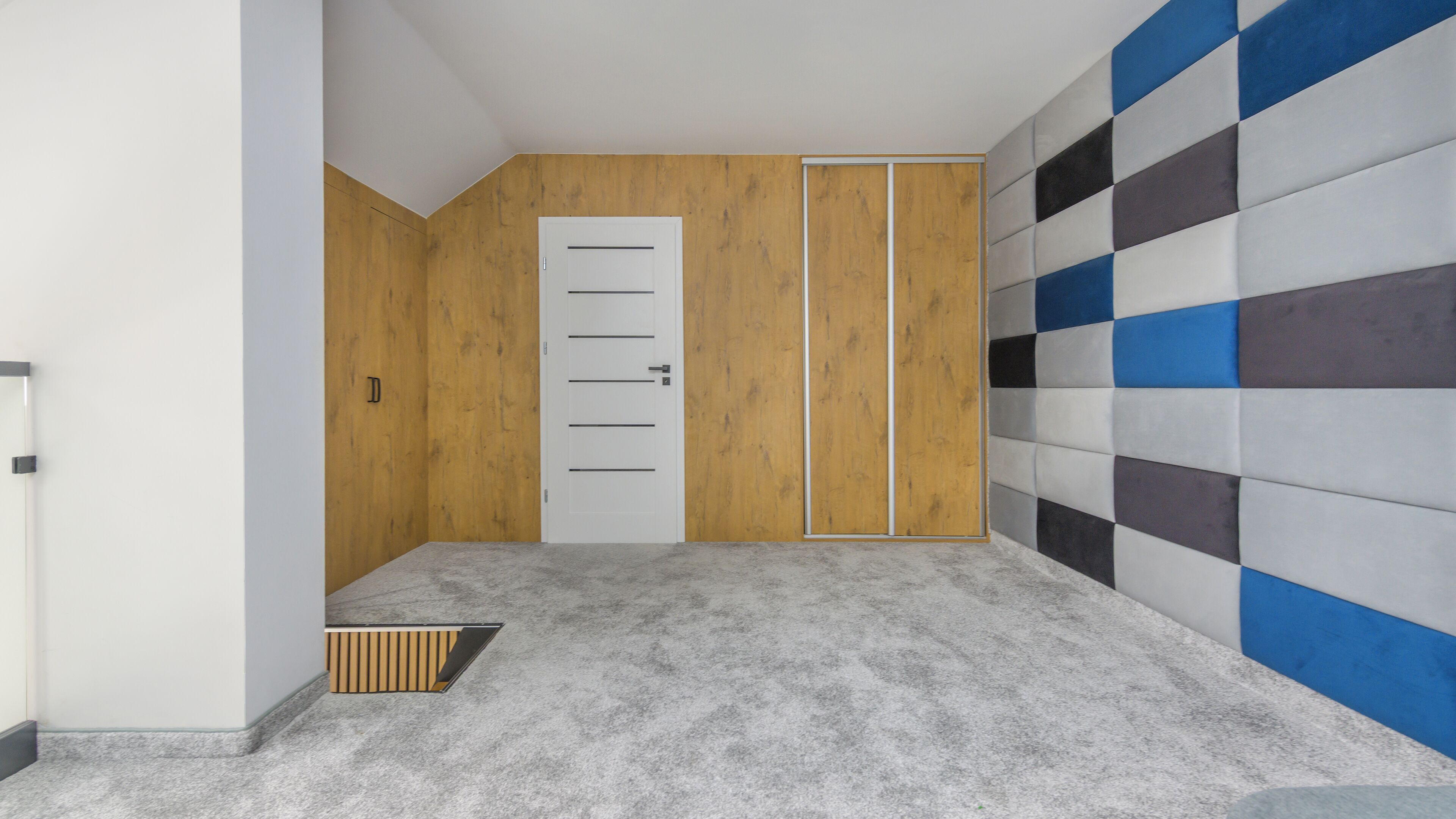 A hallway with a grey carpet, a white door, and a wall with a checkered pattern.