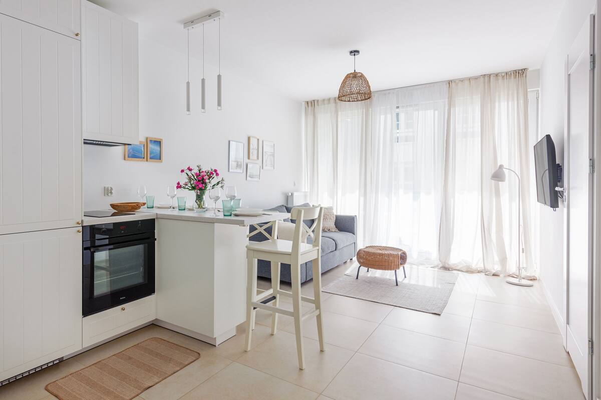 A modern kitchen with white cabinetry, a built-in oven, and a dining area with a white chair and table.
