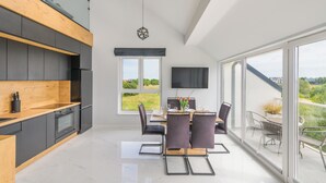 A modern kitchen with a wooden countertop, a built-in oven, and a black refrigerator. There is a dining area with a table and chairs, a TV mounted on the wall, and a large window offering a view of the outdoors.
