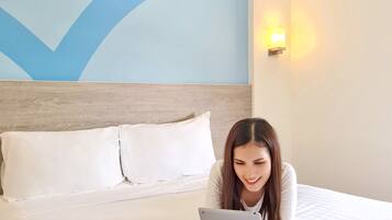 Camera d'albergo con un letto, biancheria bianca, decorazione blu alle pareti e una lampada a parete.