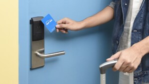 Uma pessoa utilizando um leitor de cartão para abrir uma porta com puxador metálico.