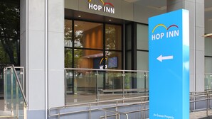 Um edifício moderno com fachada de vidro, uma placa com o texto "HOP INN" e uma seta indicativa em um letreiro azul.
