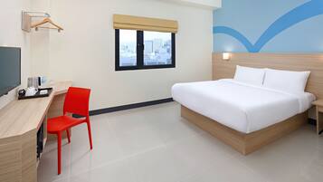 Une chambre d’hôtel avec un lit, un bureau et une chaise, une télévision et une fenêtre donnant sur des immeubles.