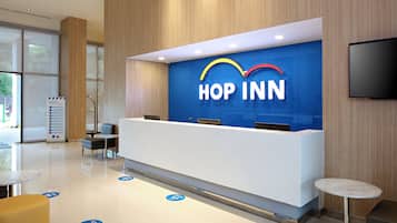 A reception desk with a 'HOP INN' sign, a flat-screen TV, and a glass partition.