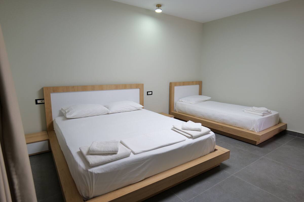 Two single beds with wooden headboards and white bedding in a modern room with grey tiled flooring.