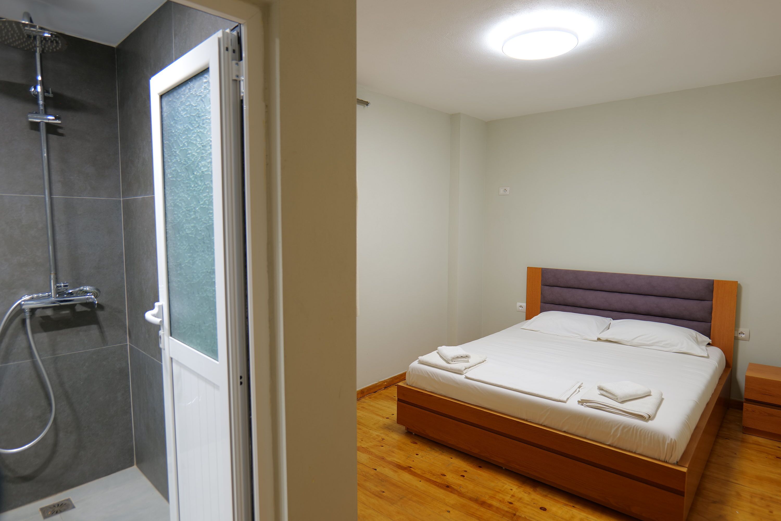 A bedroom with a wooden bed, a nightstand, and a bathroom with a shower.