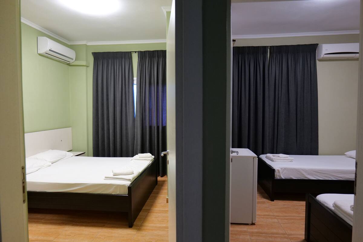 A hotel room with two single beds, a small white refrigerator, and an air conditioning unit on the wall.