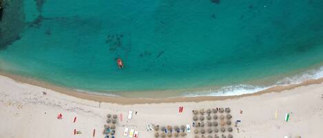 An aerial view of a beach with clear turquoise waters, a sandy shore, and various beach equipment and umbrellas.