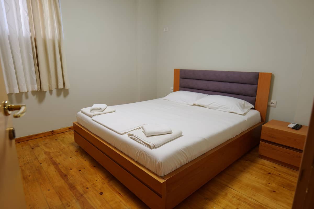 A neatly made bed with white linens and towels, a wooden headboard, and a wooden nightstand with a phone.