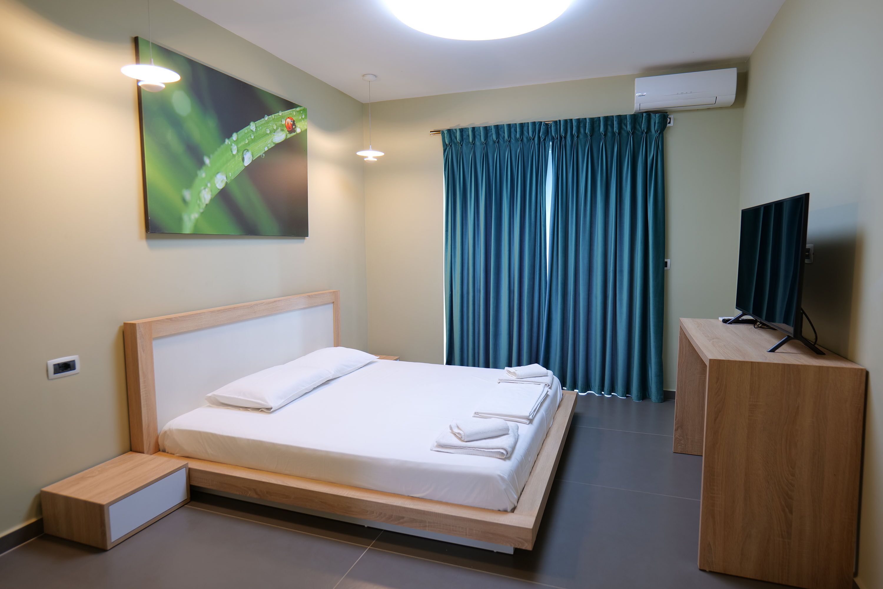 Een moderne hotelkamer met een houten bed, een flatscreen televisie en een groot raam met gordijnen.