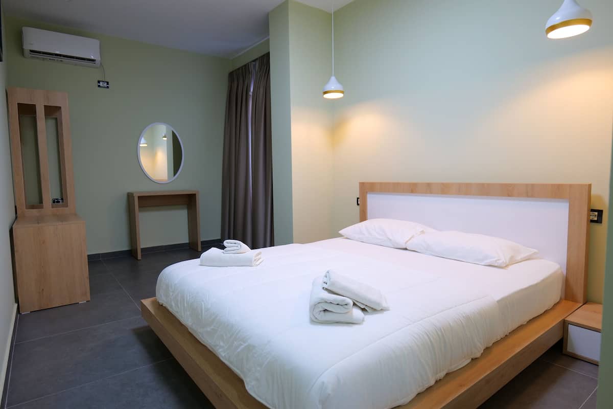 A neatly made bed with white linens and towels, a wooden headboard, and a bedside table with a lamp.