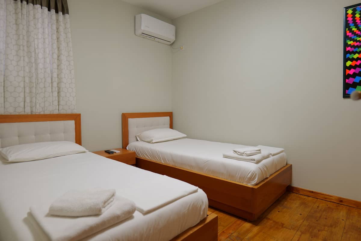 A hotel room with two beds, a wooden headboard, a nightstand, and an air conditioning unit on the wall.