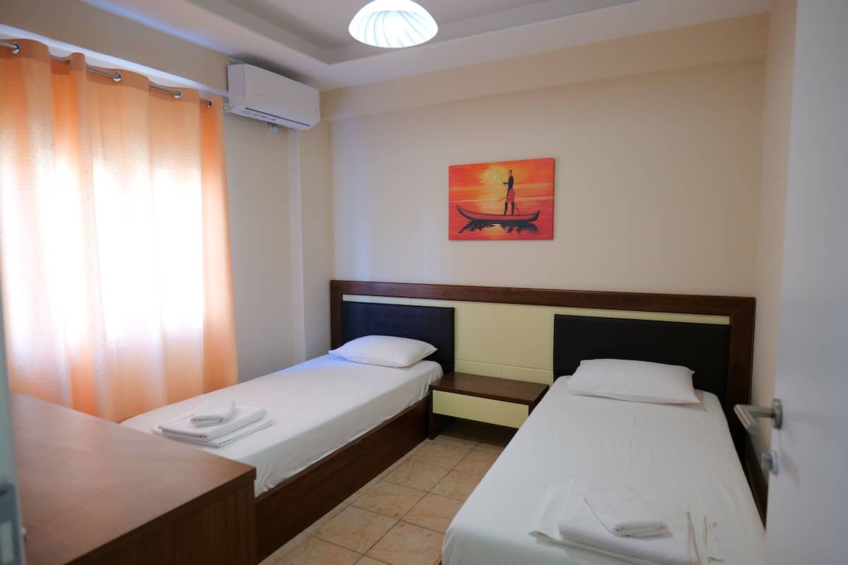 A hotel room with two single beds, a wooden desk, a small table, and a painting on the wall.