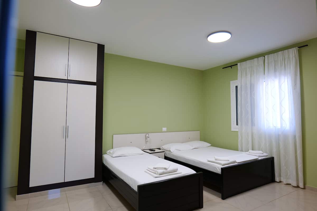 A room with two beds, a wardrobe, and a window with curtains.