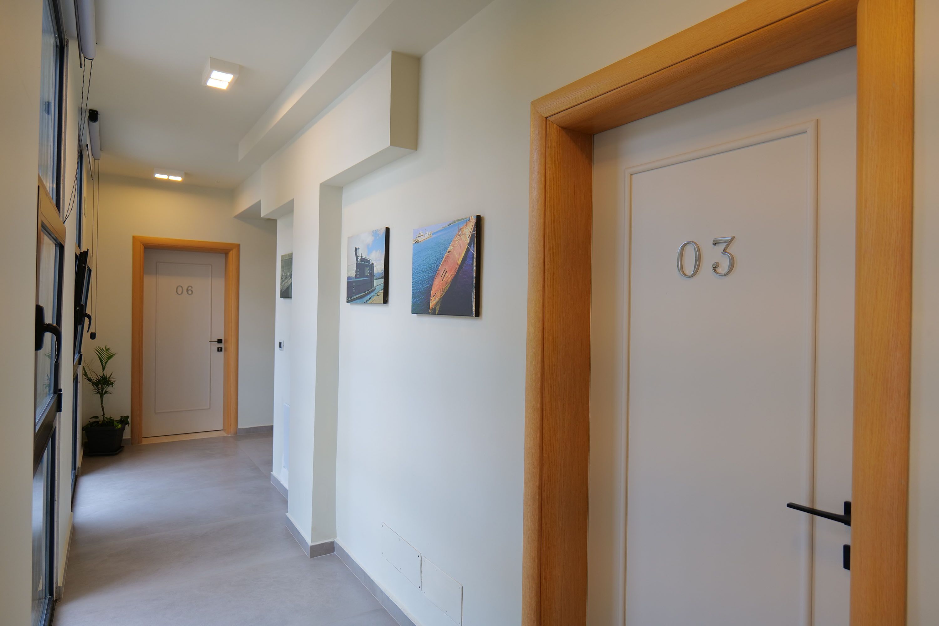 A hallway with doors numbered 03 and 06, a potted plant, and two framed pictures on the wall.