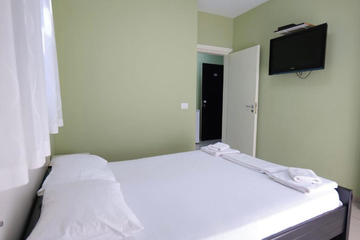 A hotel room with a bed, a television mounted on the wall, and a door leading to another room.