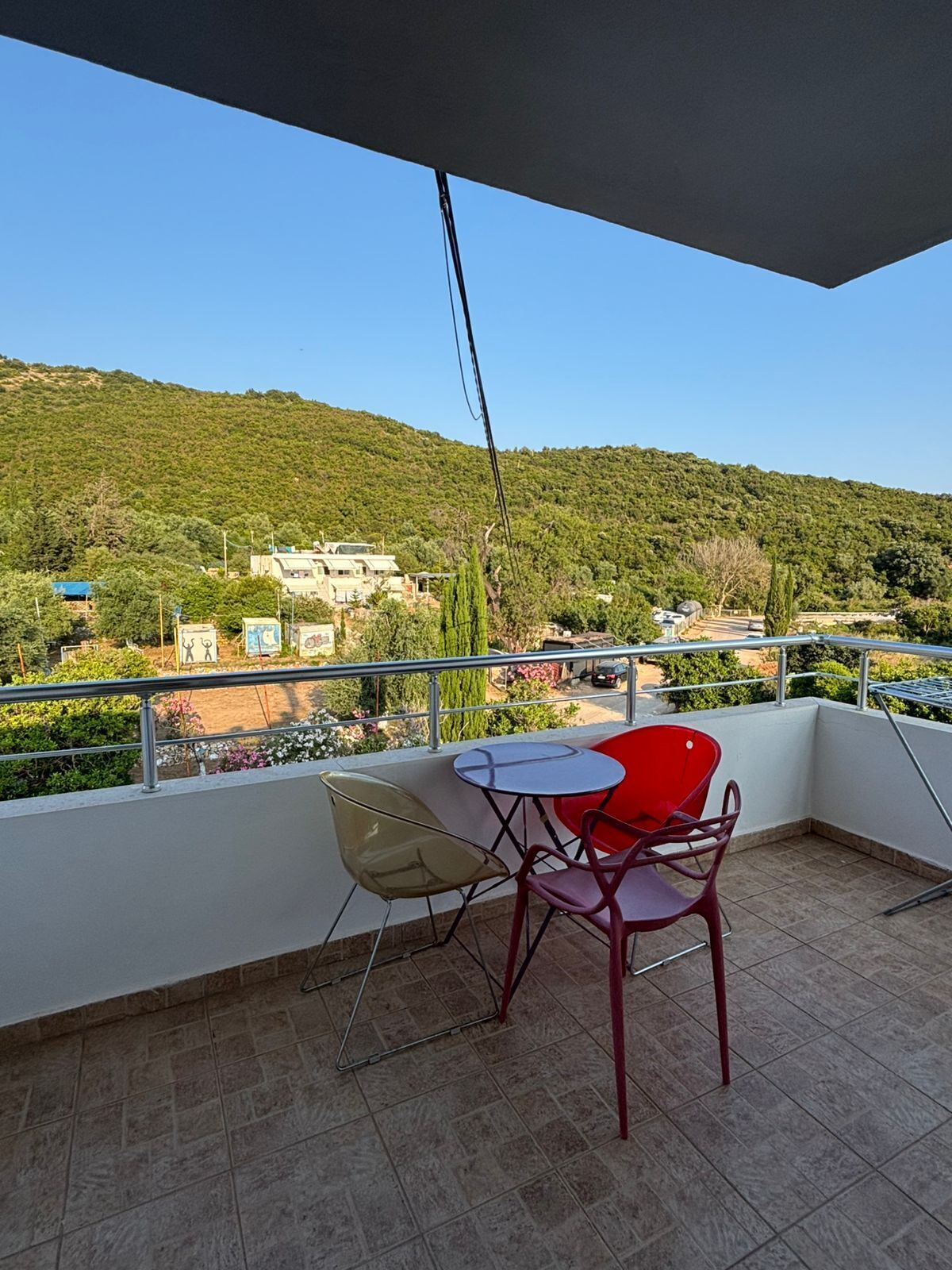 A balcony with a table and chairs, overlooking a hillside with buildings.
