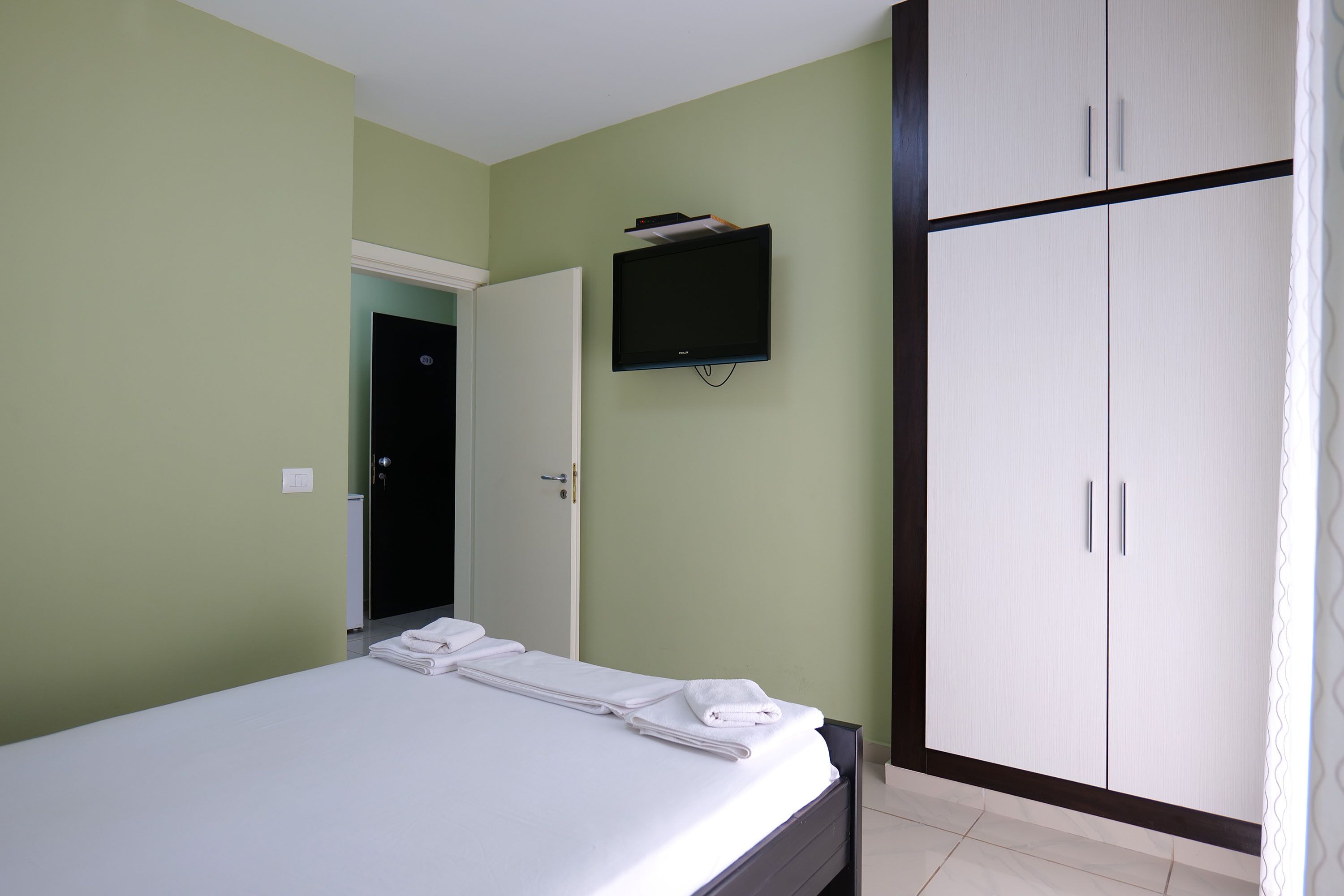 Una habitación de hotel con cama, televisión en la pared y armario.