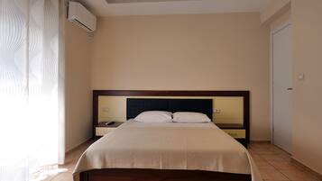 A hotel room with a bed, nightstands, a mirror, an air conditioning unit, and a door.
