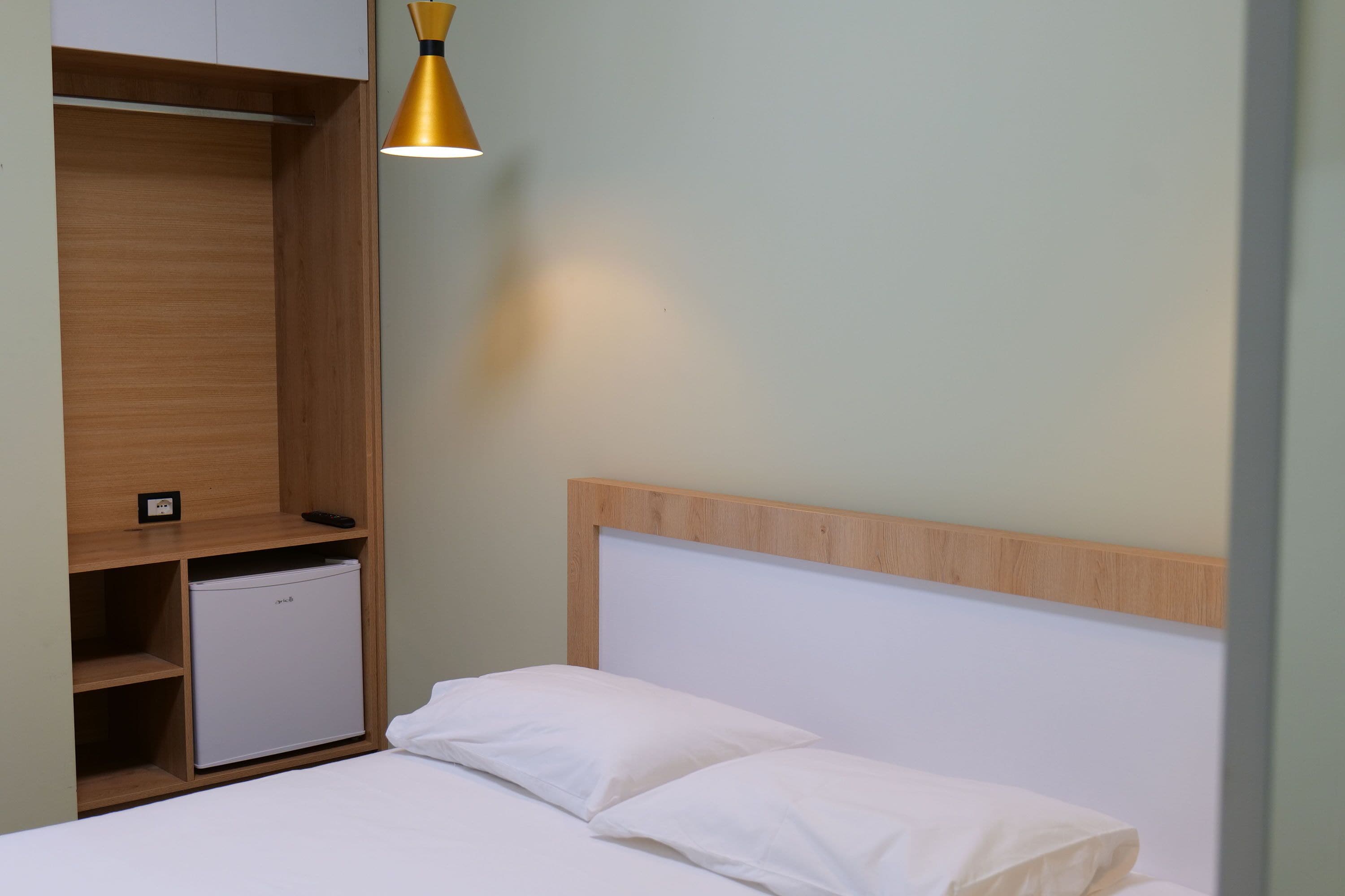 A bedroom with a bed, a wardrobe, and a small refrigerator.