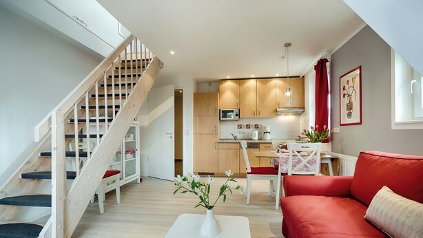 A modern apartment with a wooden staircase, a dining area with a red sofa, and a kitchen with wooden cabinets. - Quietly situated apartment for up to 2 p. + infant, sauna, WLAN, balcony, bicycle shed (Prerow)