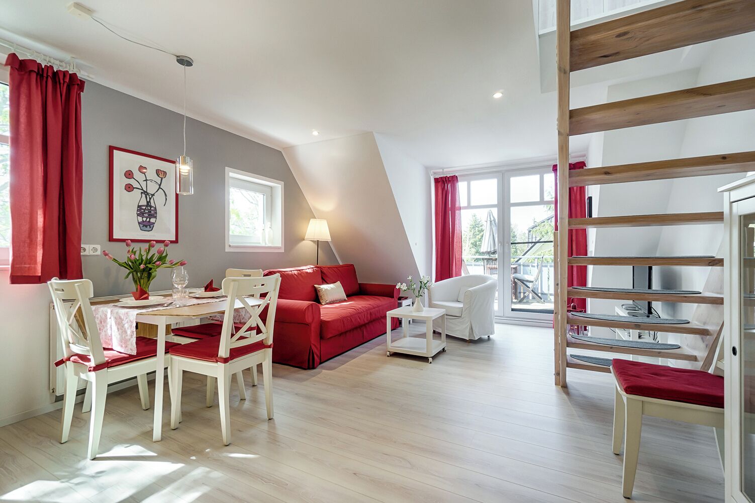 A modern living room with a dining area, red and white furniture, a staircase, and large windows.