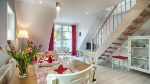 A dining area with a wooden table set for four, a vase of tulips, and a modern pendant light. - Quietly situated apartment for up to 2 p. + infant, sauna, WLAN, balcony, bicycle shed (Prerow)