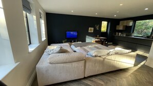 A modern bedroom with a large bed, a TV, a small table, and a view of greenery outside. - Nestled in a grand private estate, near woodlands, easy access London (Kingston upon Thames)