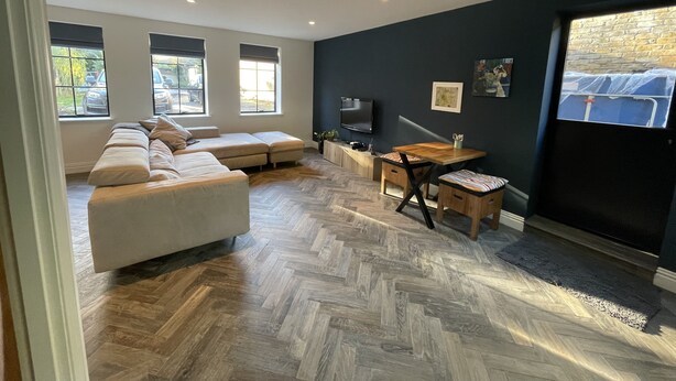 A modern living room with a sectional sofa, a dining table with chairs, a flat-screen TV, and a herringbone-patterned floor. - Nestled in a grand private estate, near woodlands, easy access London (Kingston upon Thames)