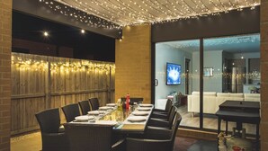 An outdoor dining area with a long table set for six, surrounded by wicker chairs.