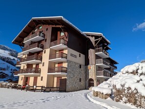 Ein mehrstöckiges Hotel mit Balkonen, einer steinernen Fassade und einer Skipiste im Hintergrund.