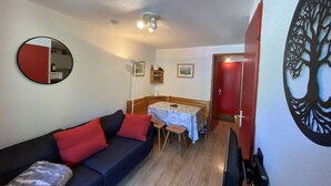 A compact living space with a sofa, a dining table, a TV, and a red door. - Cozy apartment 3-5 pers, pool, near slopes, village center (Arêches-Beaufort)