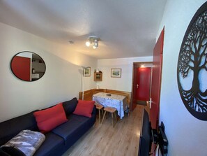 Ein kompakter Wohnraum mit Sofa, Esstisch, Fernseher und einer roten Tür.