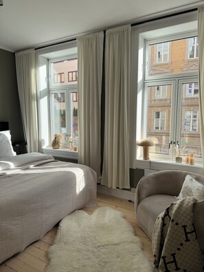 Une chambre à coucher avec un lit, une chaise, un tapis et une fenêtre avec des rideaux.